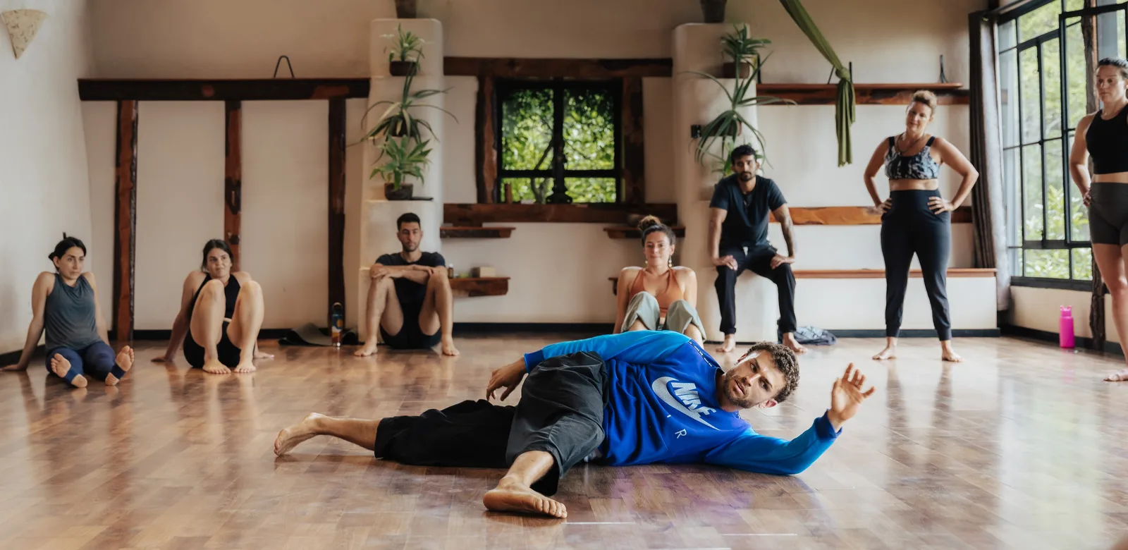 Omar demonstrating a floor movement while a group of workshop participants sit and stand around the studio watching